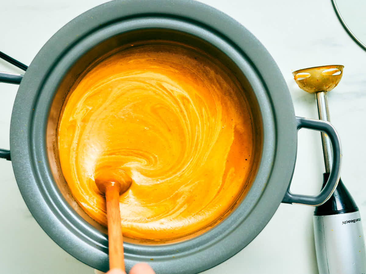 Stirring cream into Slow Cooker Pumpkin Soup after blending.