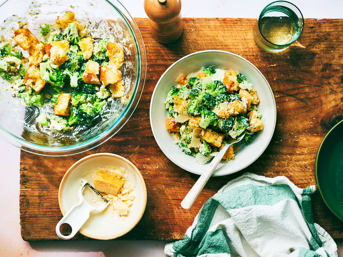 Bowls of Broccoli Caesar Salad on a dinner table with Parmesan cheese.