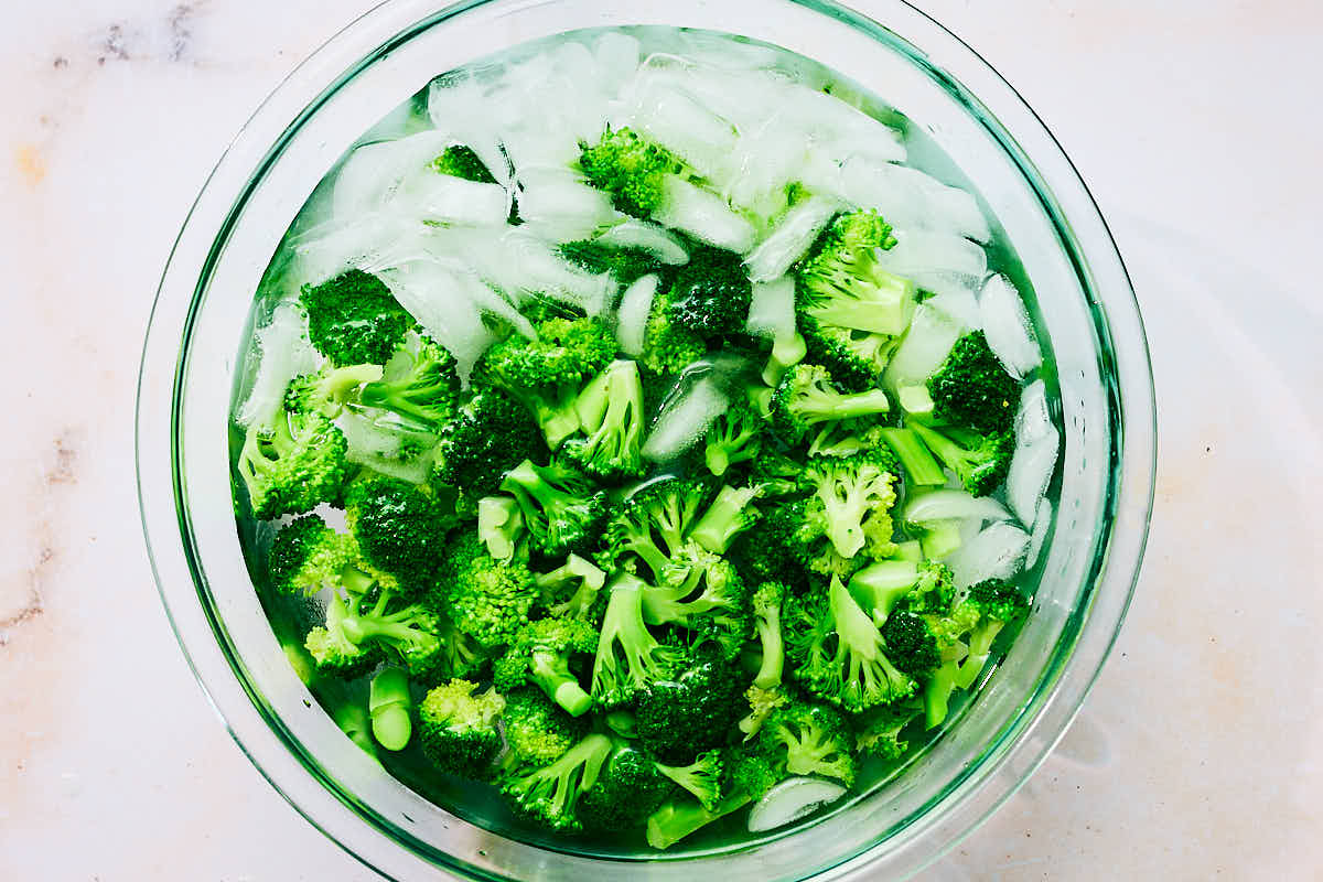 Blanched broccoli florets in a bowl of ice water.