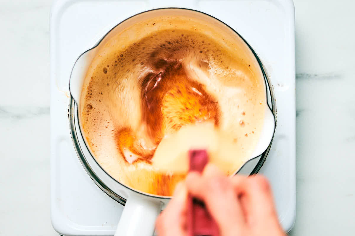 Brown butter being stirred in a pot on the stove.
