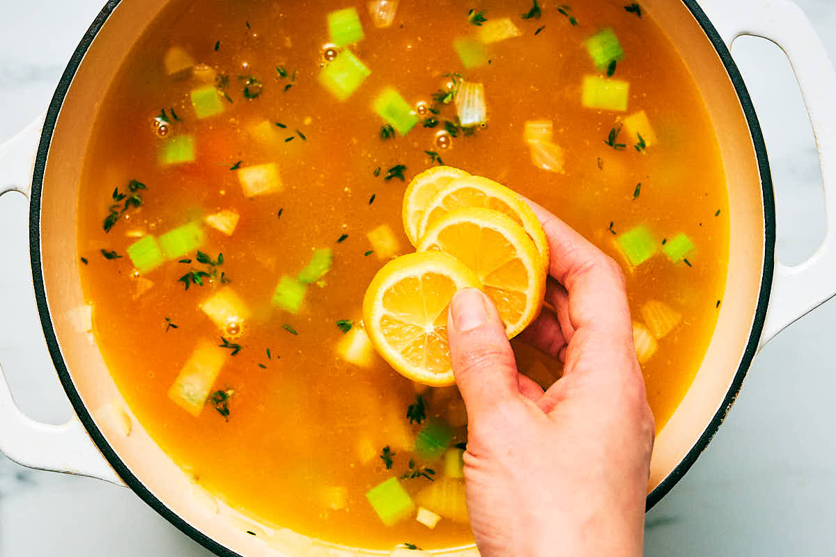 Adding sliced lemons to a pot of vegetarian lemon rice soup.