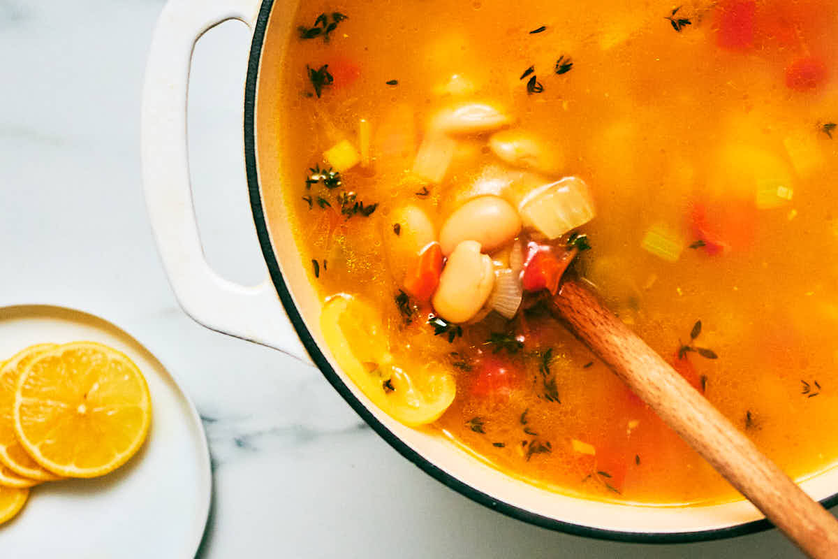 Stirring rice and white beans into a pot of lemon and veggie soup.
