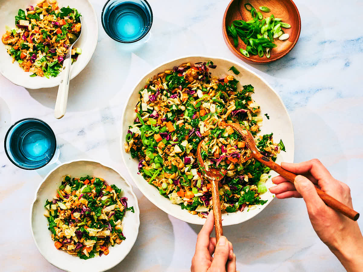 Asian Crunch Salad with Peanut Tofu being scooped out of a serving bowl at a dinner table.