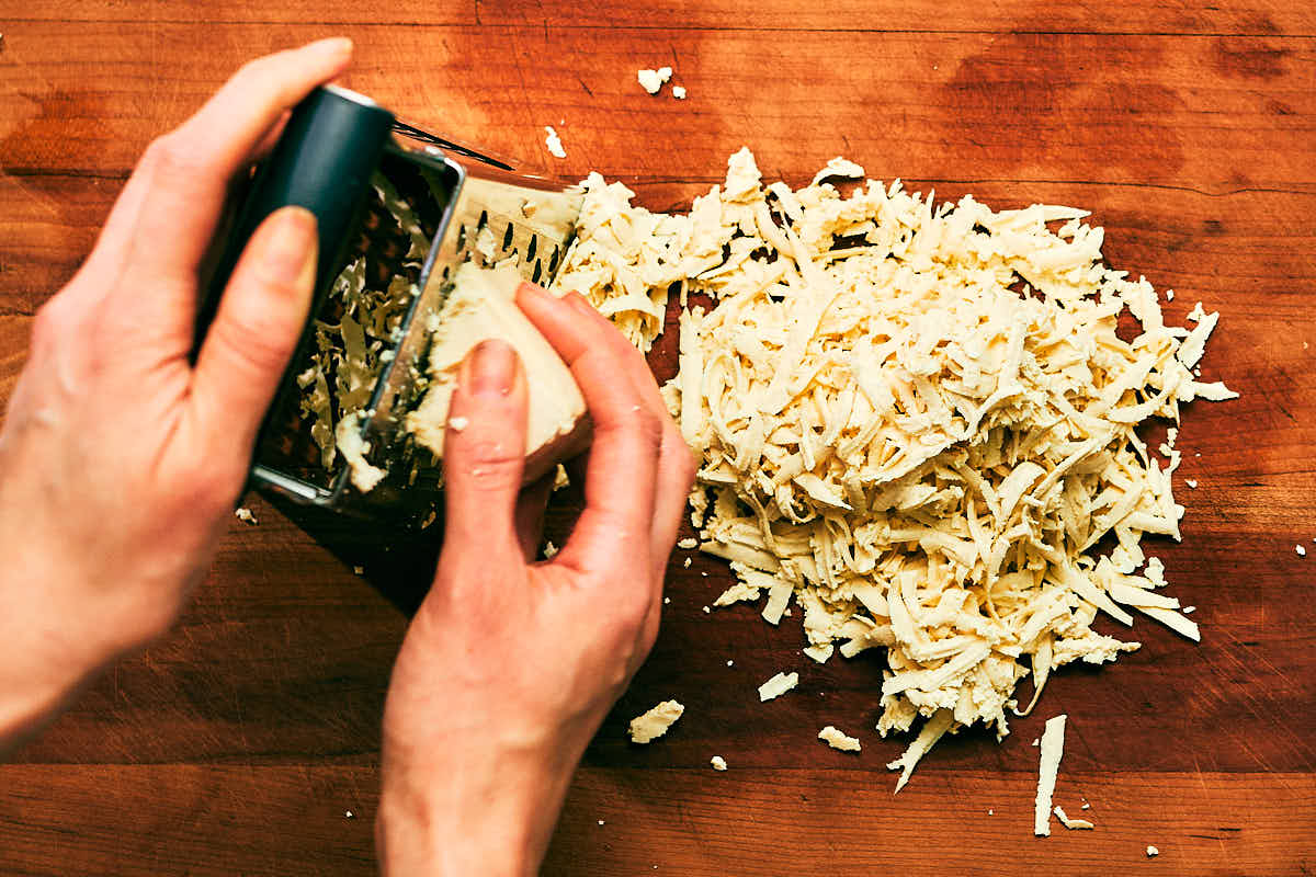Extra firm tofu being shredded on a cheese grater.