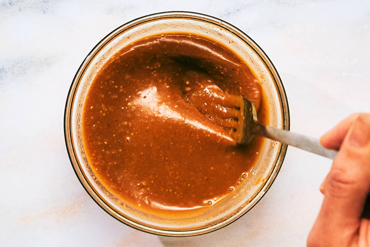 Creamy peanut butter sauce being whisked in a glass jar.