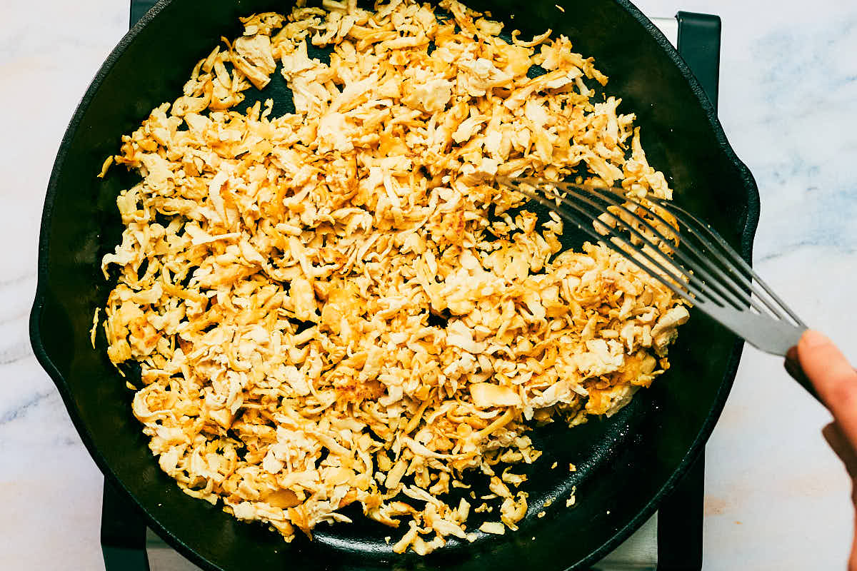 Shredded tofu being sauteed in a skillet until crisp on the edges.