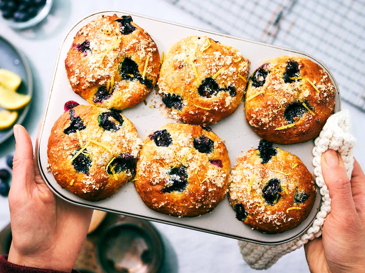 Hands holding a muffin tin with fresh Blueberry Cottage Cheese Muffins with lemon.