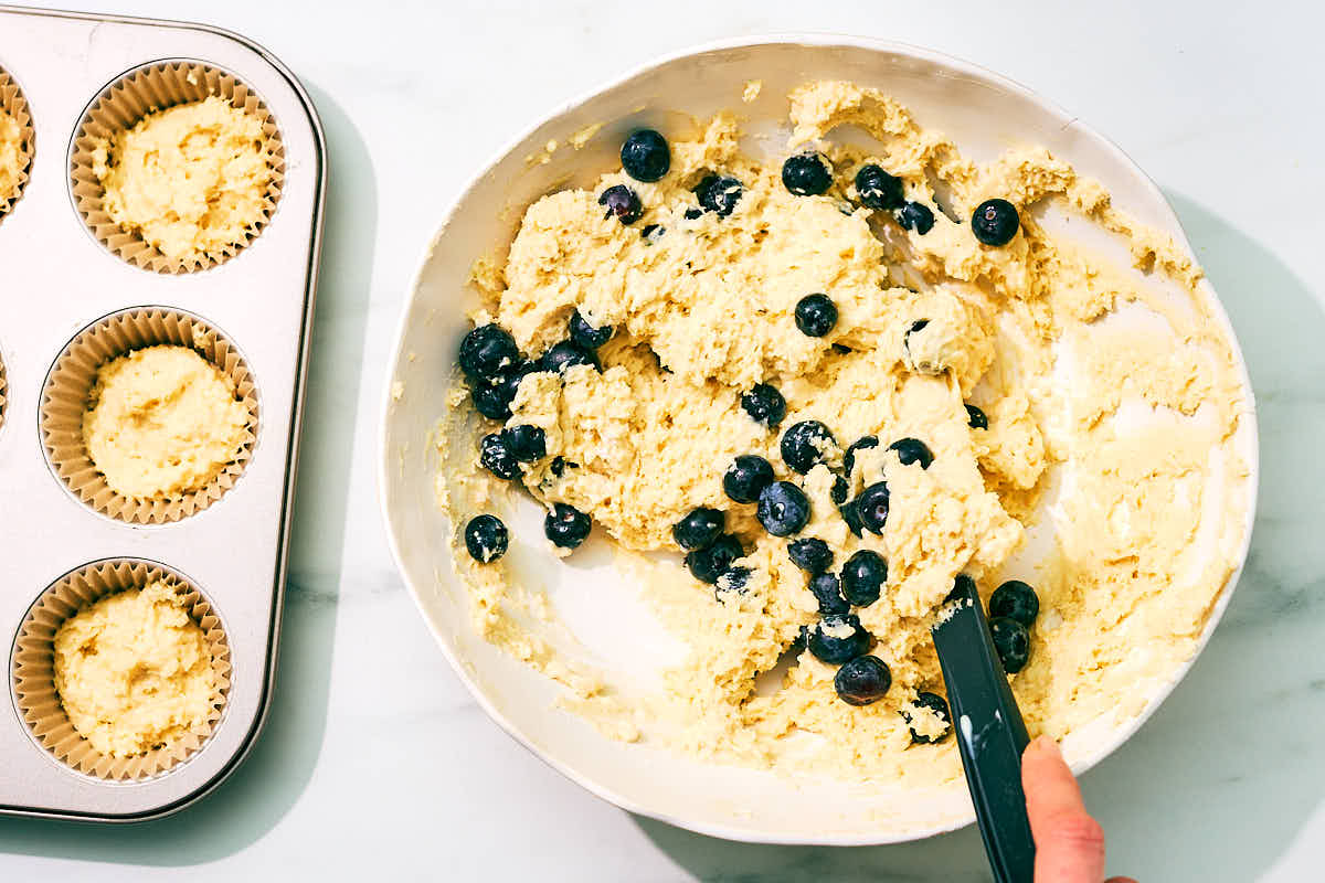 Fresh blueberries being mixed into a bowl of cottage cheese muffin batter.