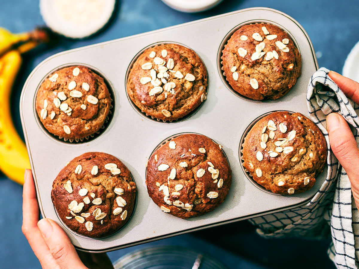 Hands holding Banana Cottage Cheese Muffins in a baking tin.