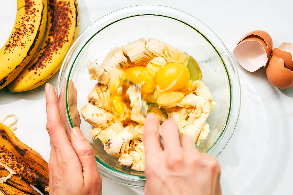 Banana being mashed with eggs in a glass bowl.
