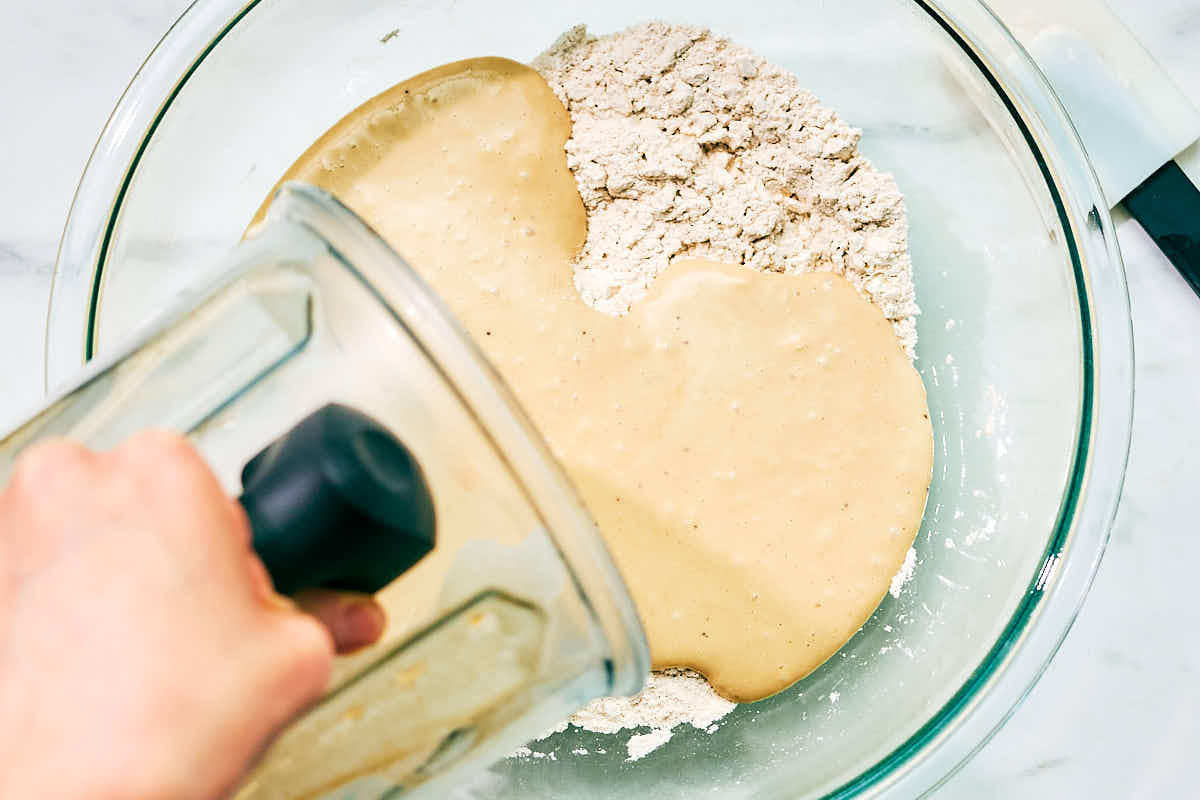 Wet ingredients being poured from blender into bowl of dry ingredients.