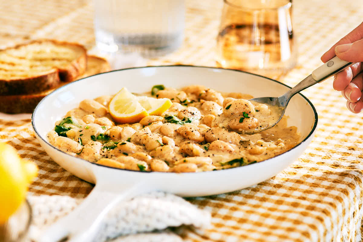 A spoon scooping Creamy Lemon Butter Beans out of a skillet to serve.
