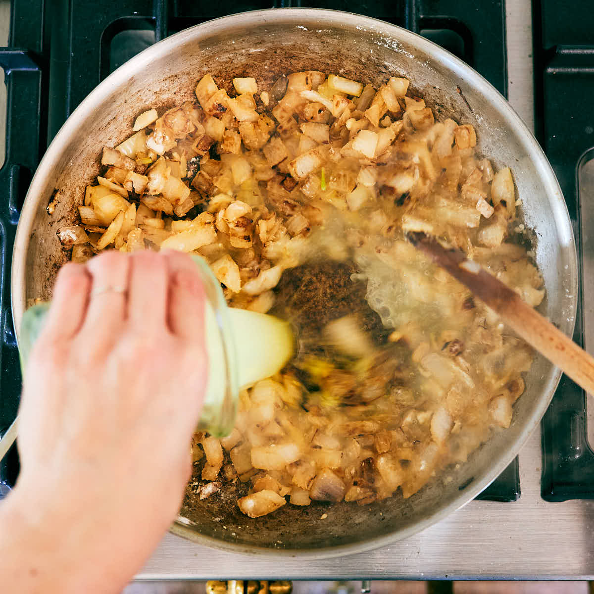 Vegetable stock being poured into a skillet with onion and garlic.