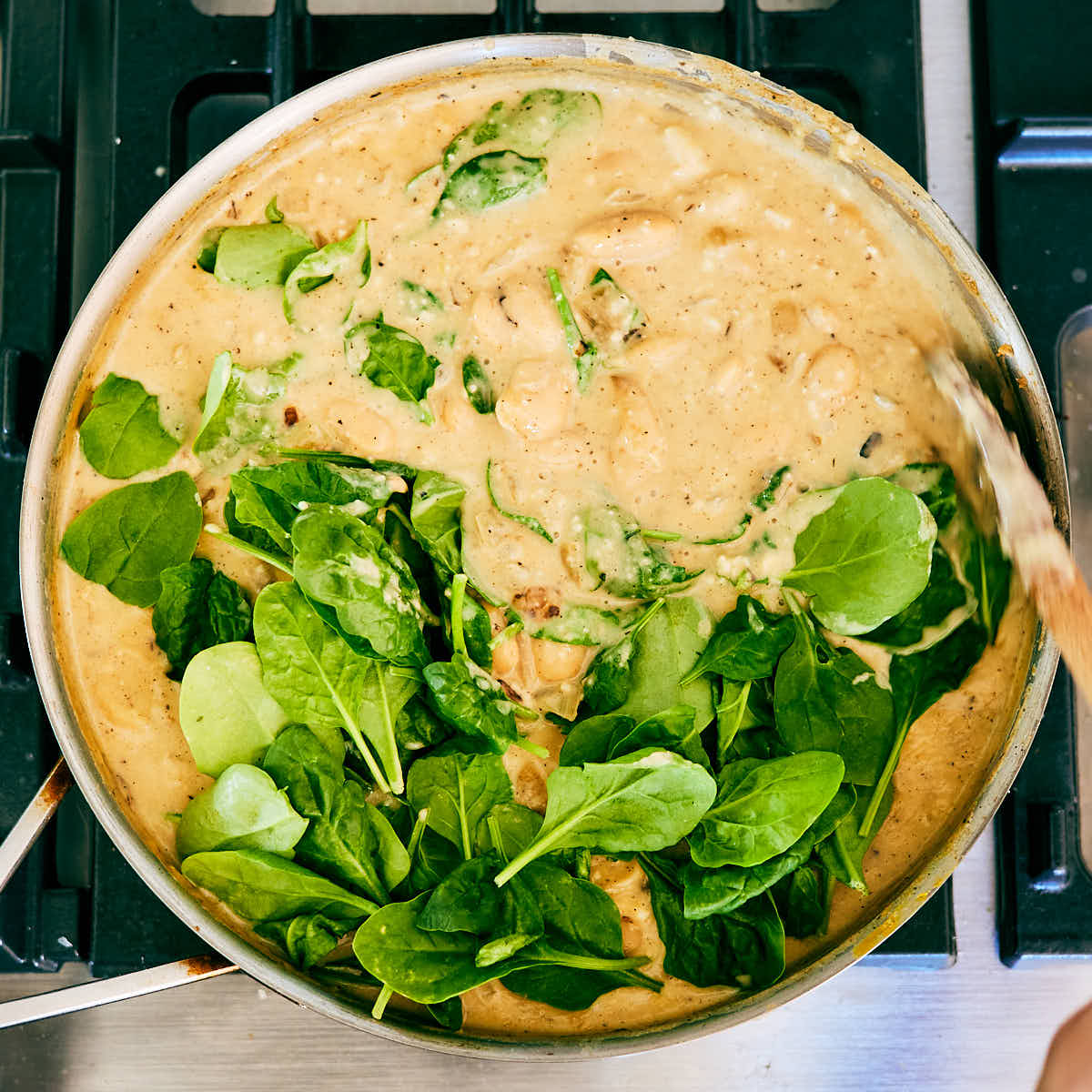 Baby spinach being stirred into a skillet of Creamy Lemon Butter Beans before serving.