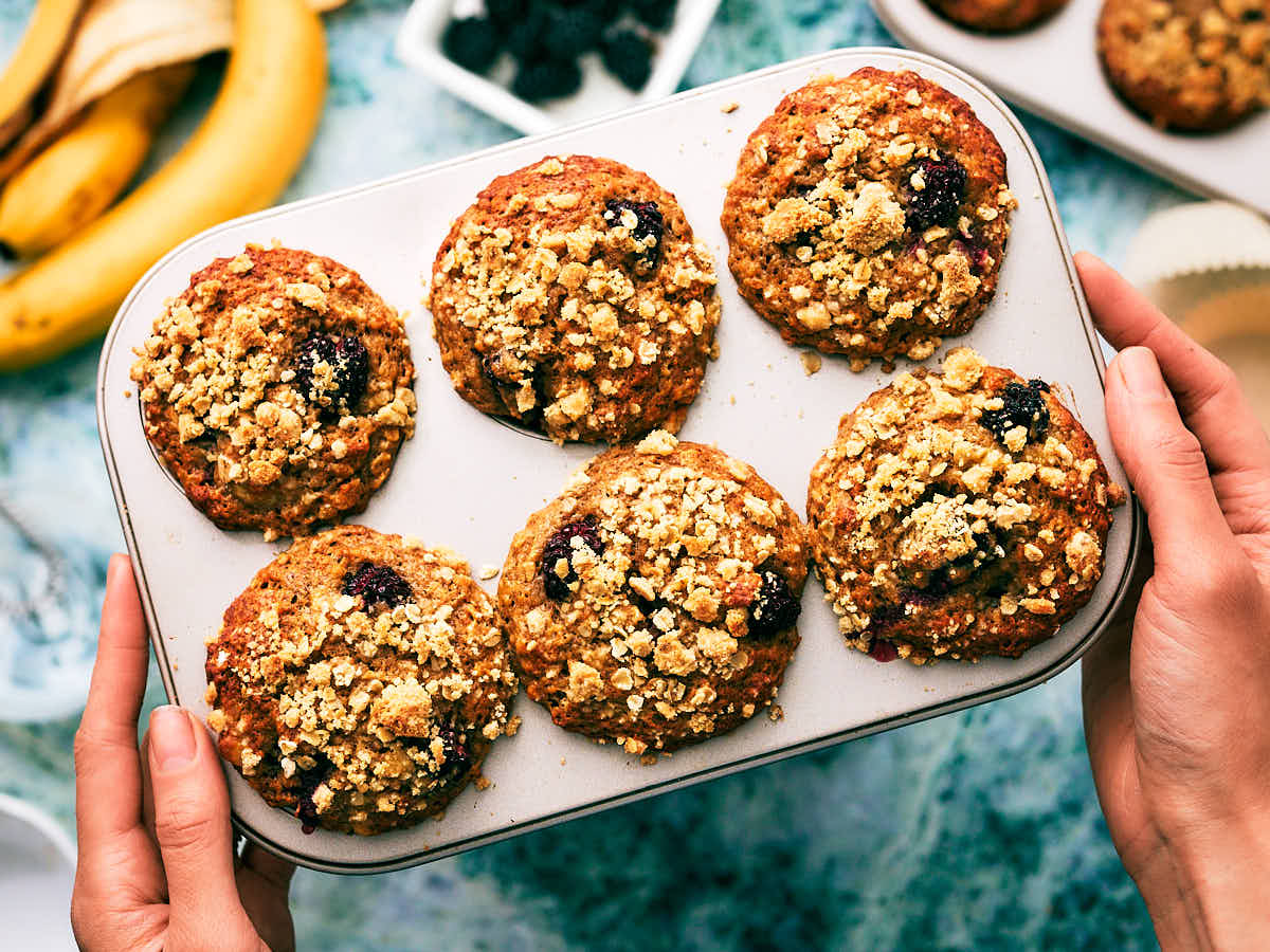 A woman's hands holding a muffin tin with freshly baked Banana Blackberry Muffins.