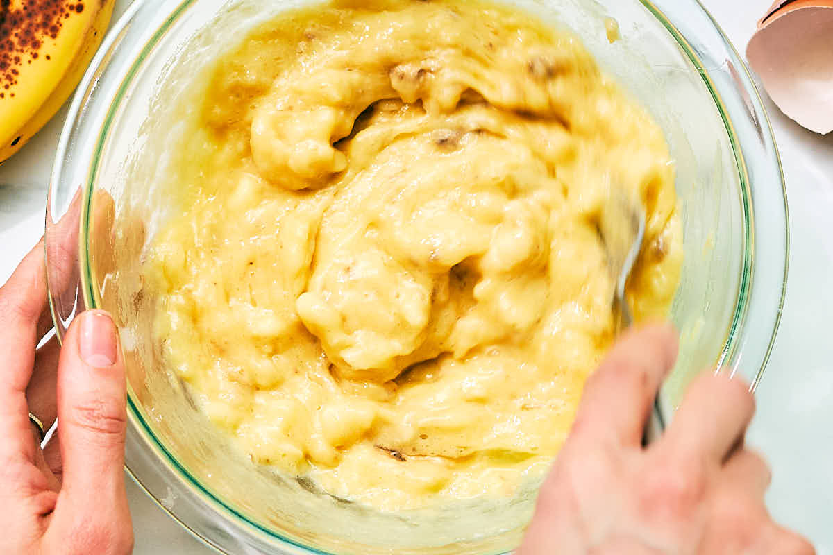 Mixing bananas and eggs in a bowl for banana muffins.