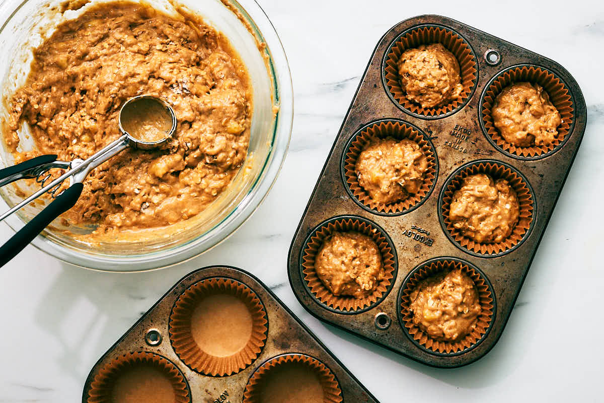 Banana muffin batter being scooped into muffin tin.