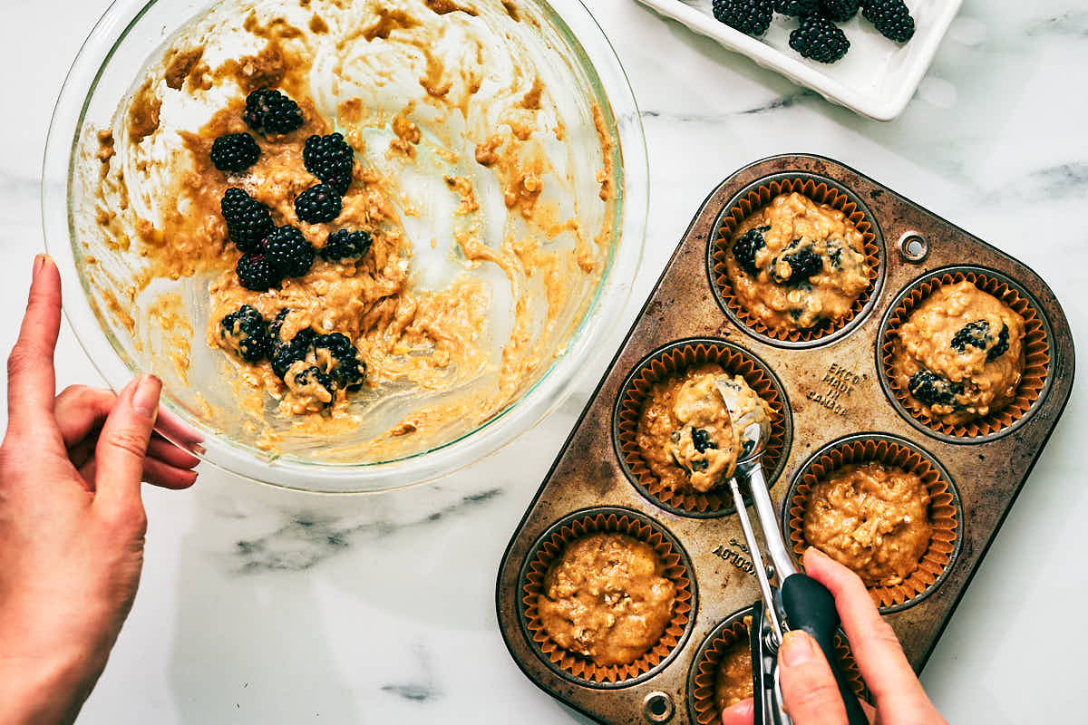Blackberry banana muffin batter being scooped into muffin tin.