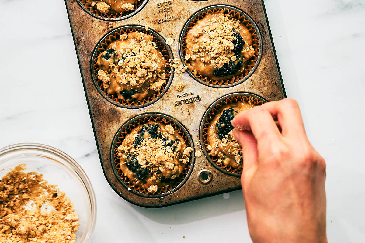 Oat streusel being sprinkled on top of muffins before baking.