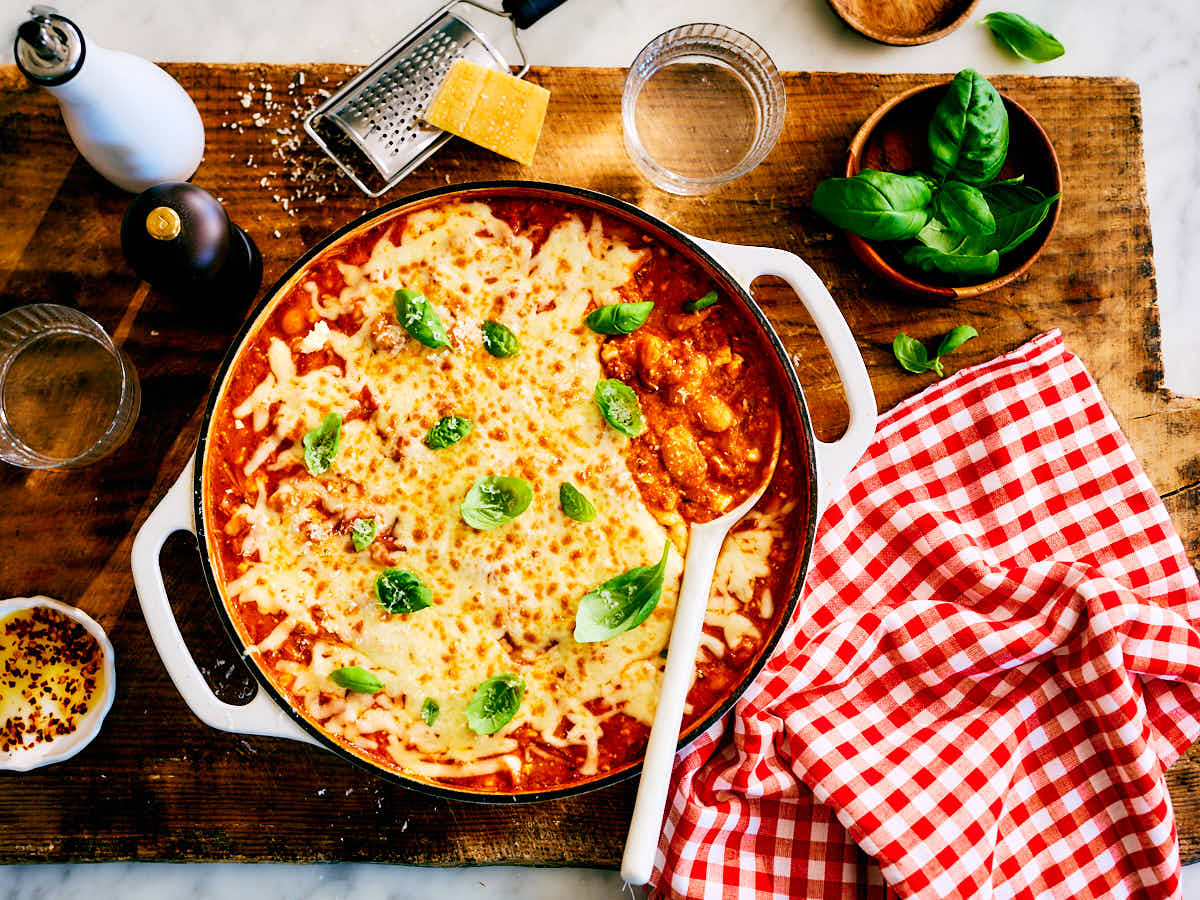 High protein pizza beans in a skillet with serving spoon, chili oil, and cheese.
