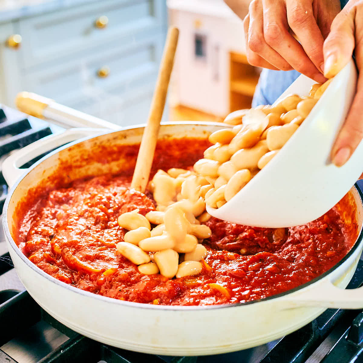 Butter beans being added to marinara sauce in skillet for pizza beans.
