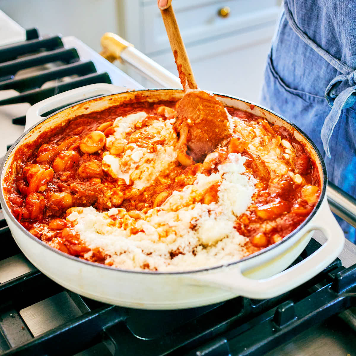 Cottage cheese and parmesan being stirred into a skillet of pizza beans.