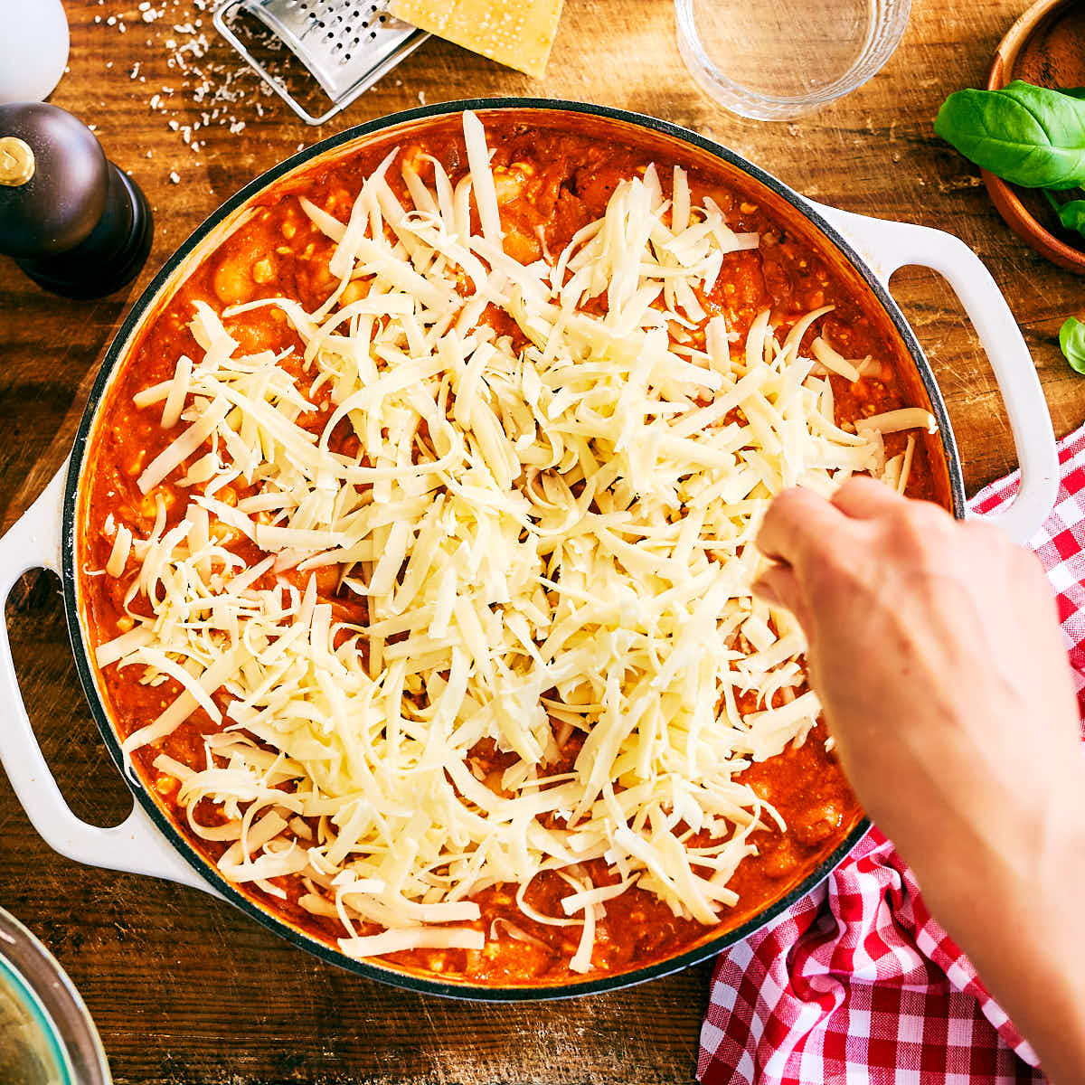 Shredded mozzarella being sprinkled over skillet of pizza beans before oven.