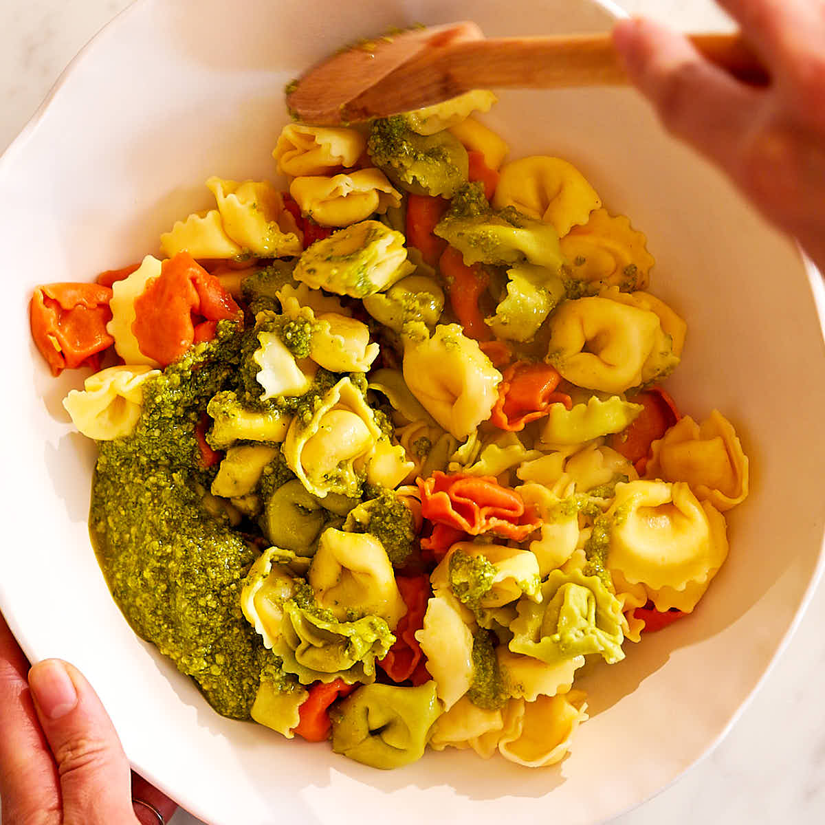 Cheese tortellini being tossed with pesto in a bowl.