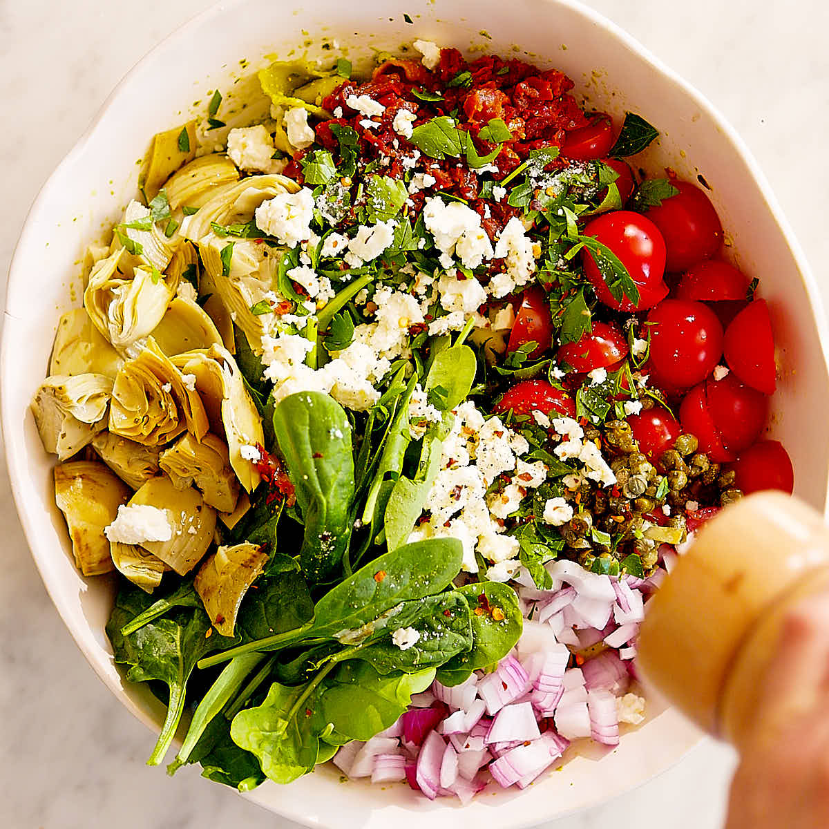 Pesto Tortellini Pasta Salad with feta, tomatoes, artichokes in a bowl.