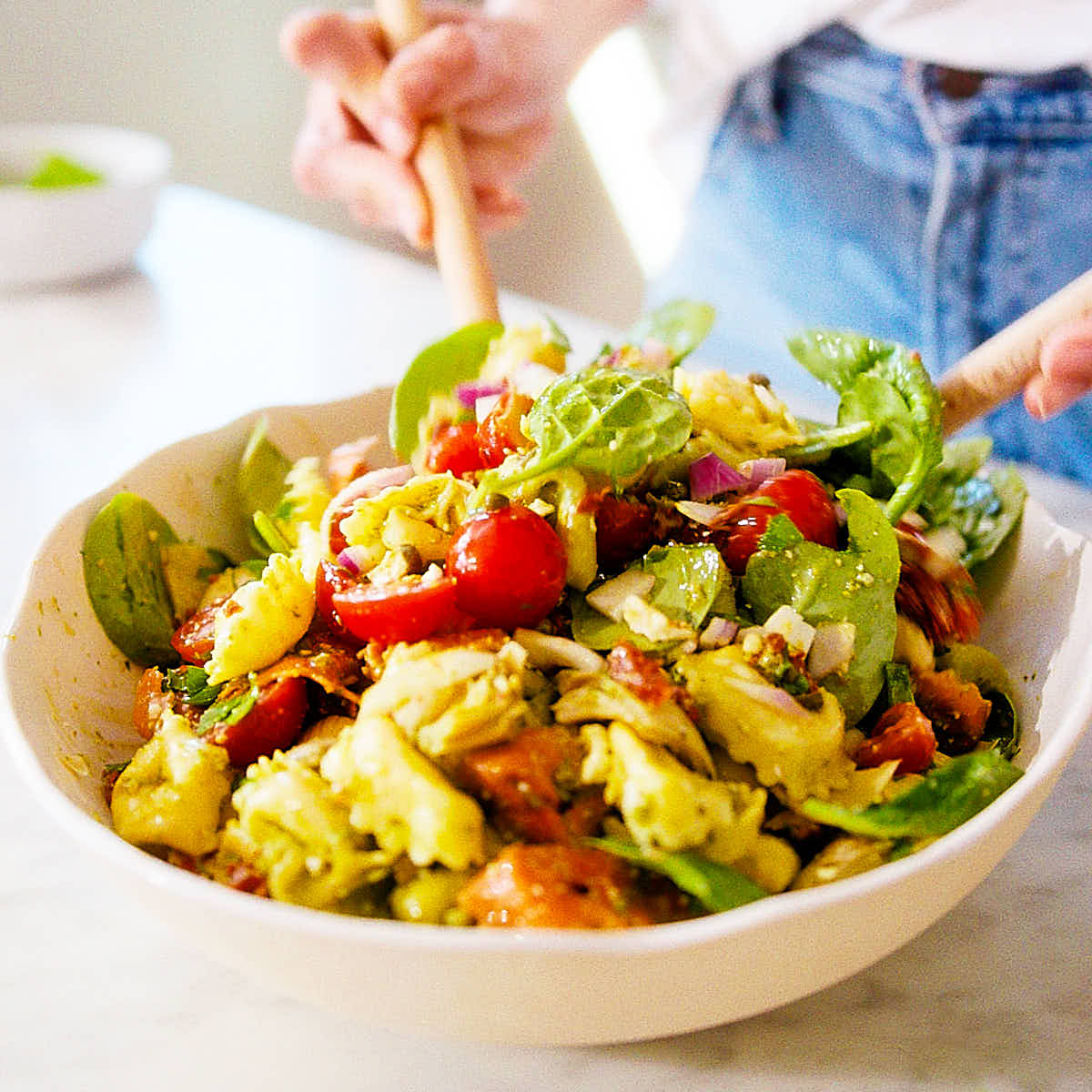 Vegetarian Pesto Tortellini Pasta Salad being tossed in a bowl.