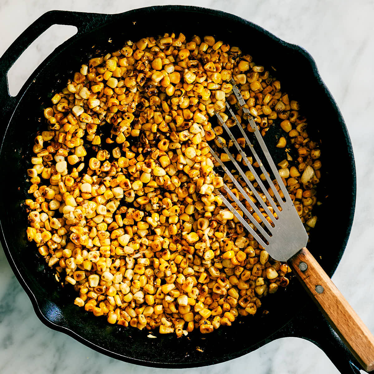 Corn kernels being seared in a cast iron skillet.