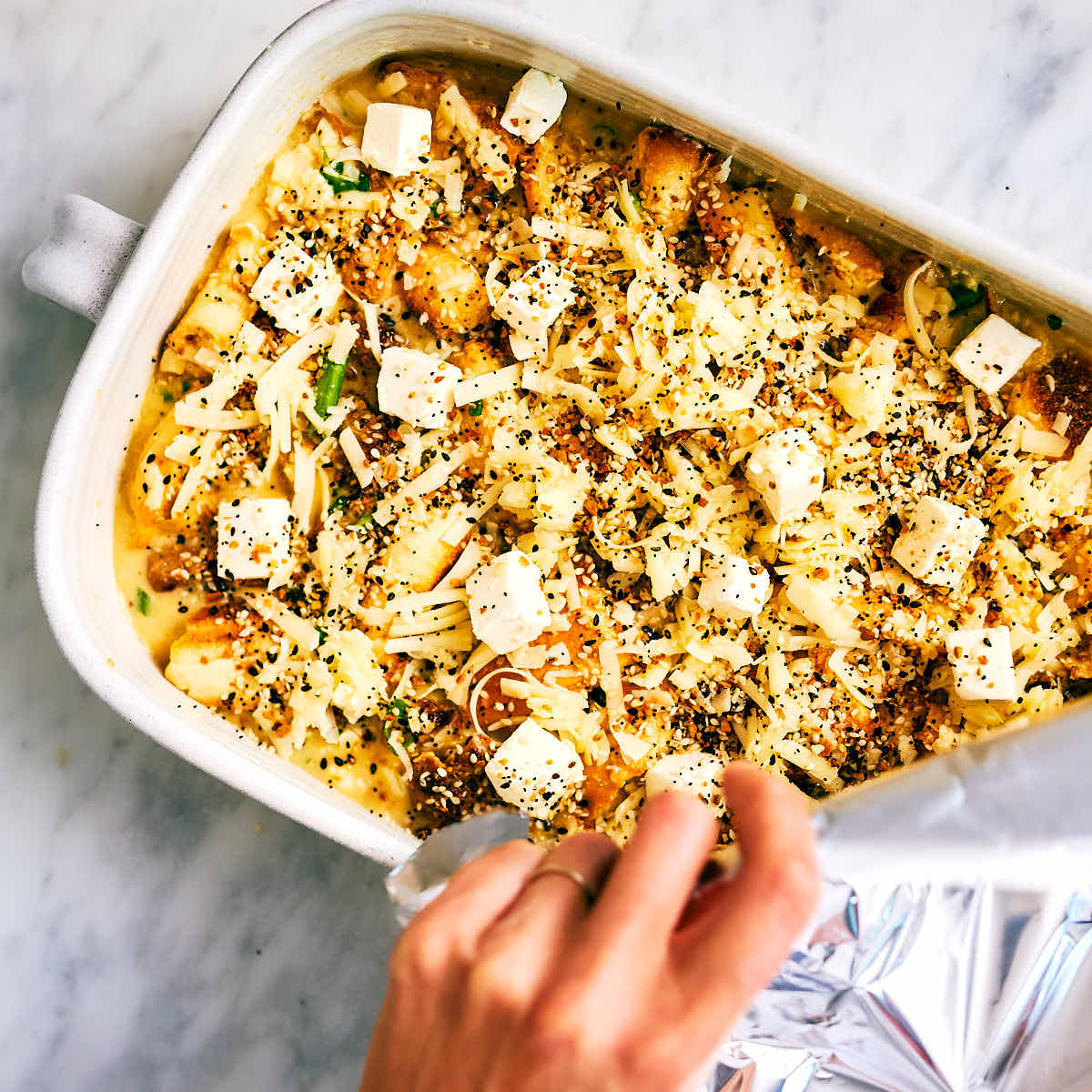 Breakfast bagel casserole being covered with foil before going into the oven.