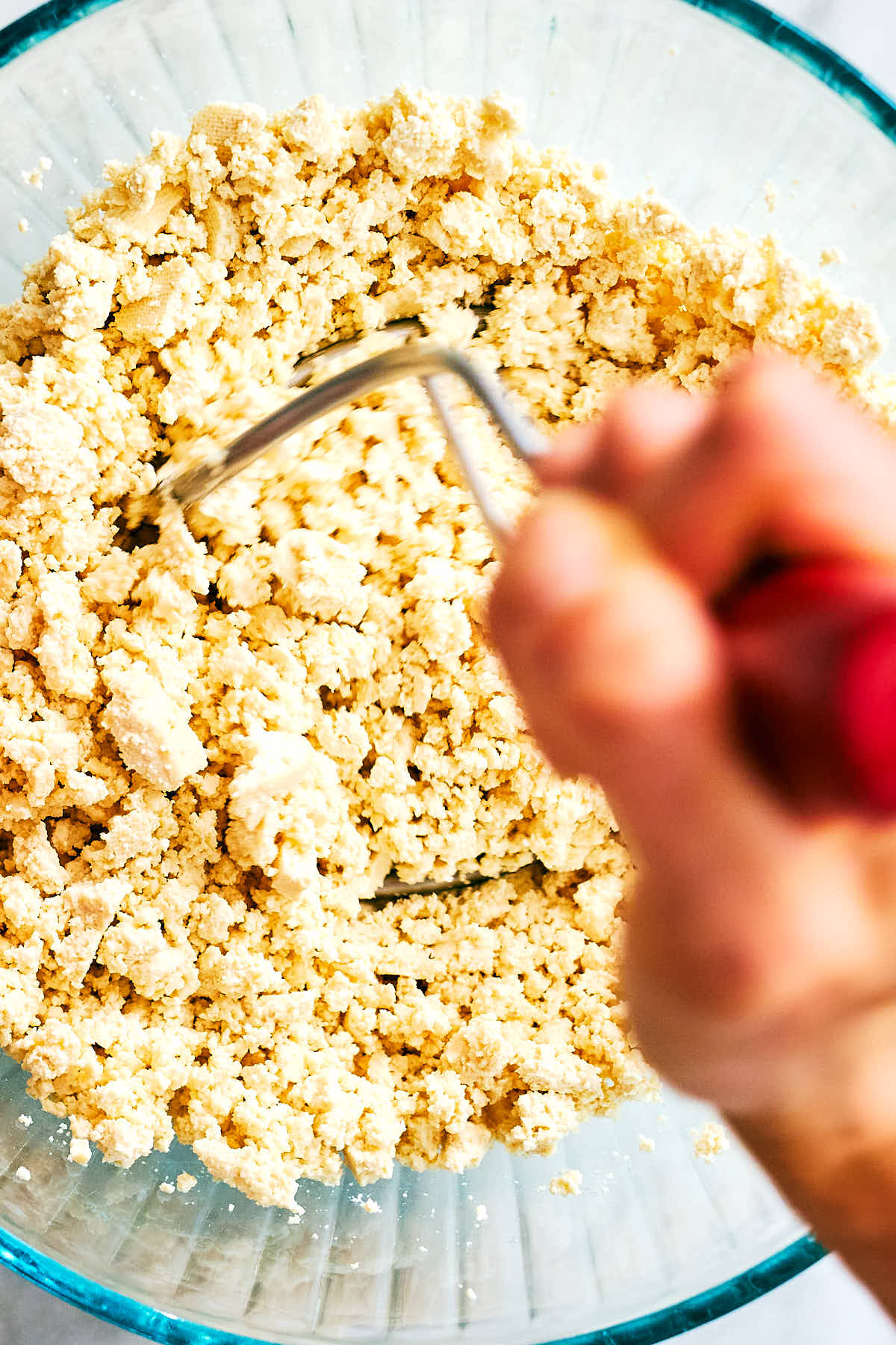 A potato masher being used to crumble tofu.