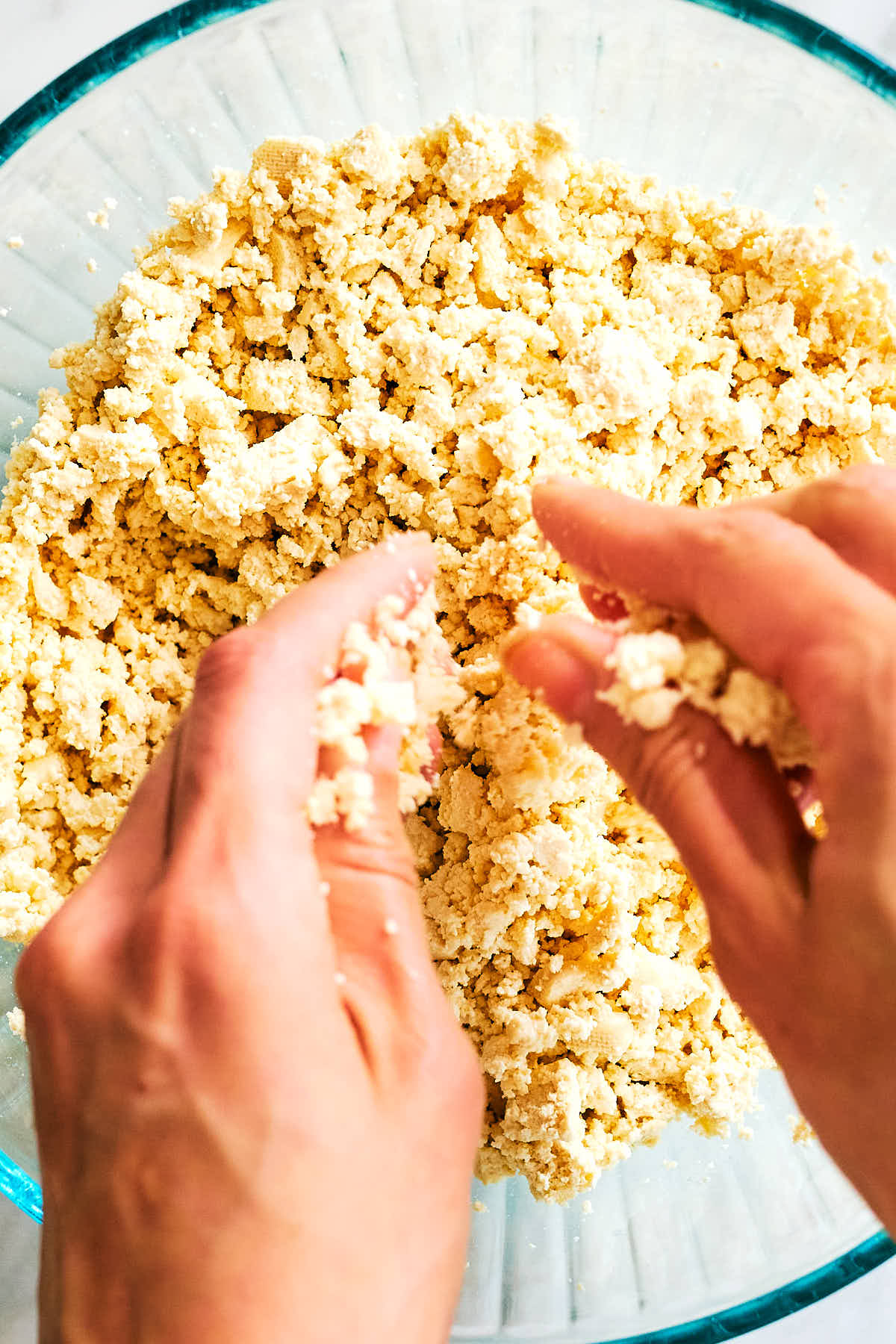 Hands crumbling tofu into a bowl.