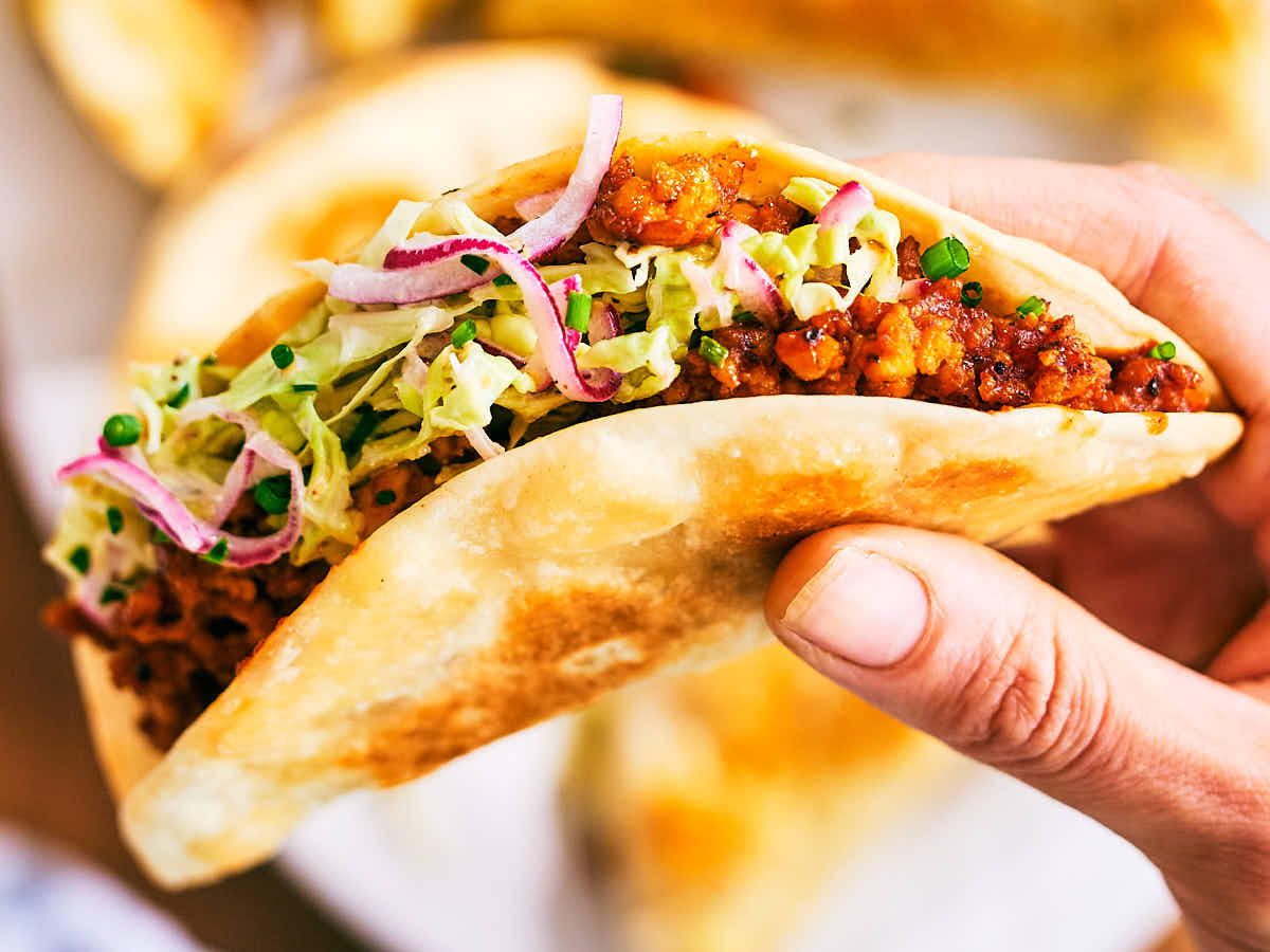 A hand holding Evergreen Kitchen's Crispy Sheet Pan Taco with Barbecue Tofu.