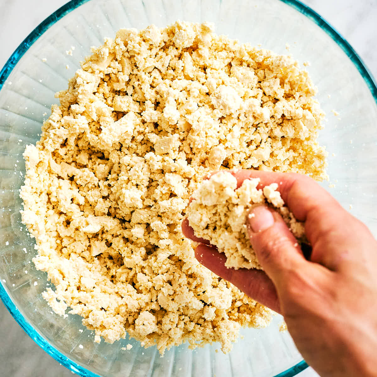 Hands crumbling extra firm tofu in a bowl.