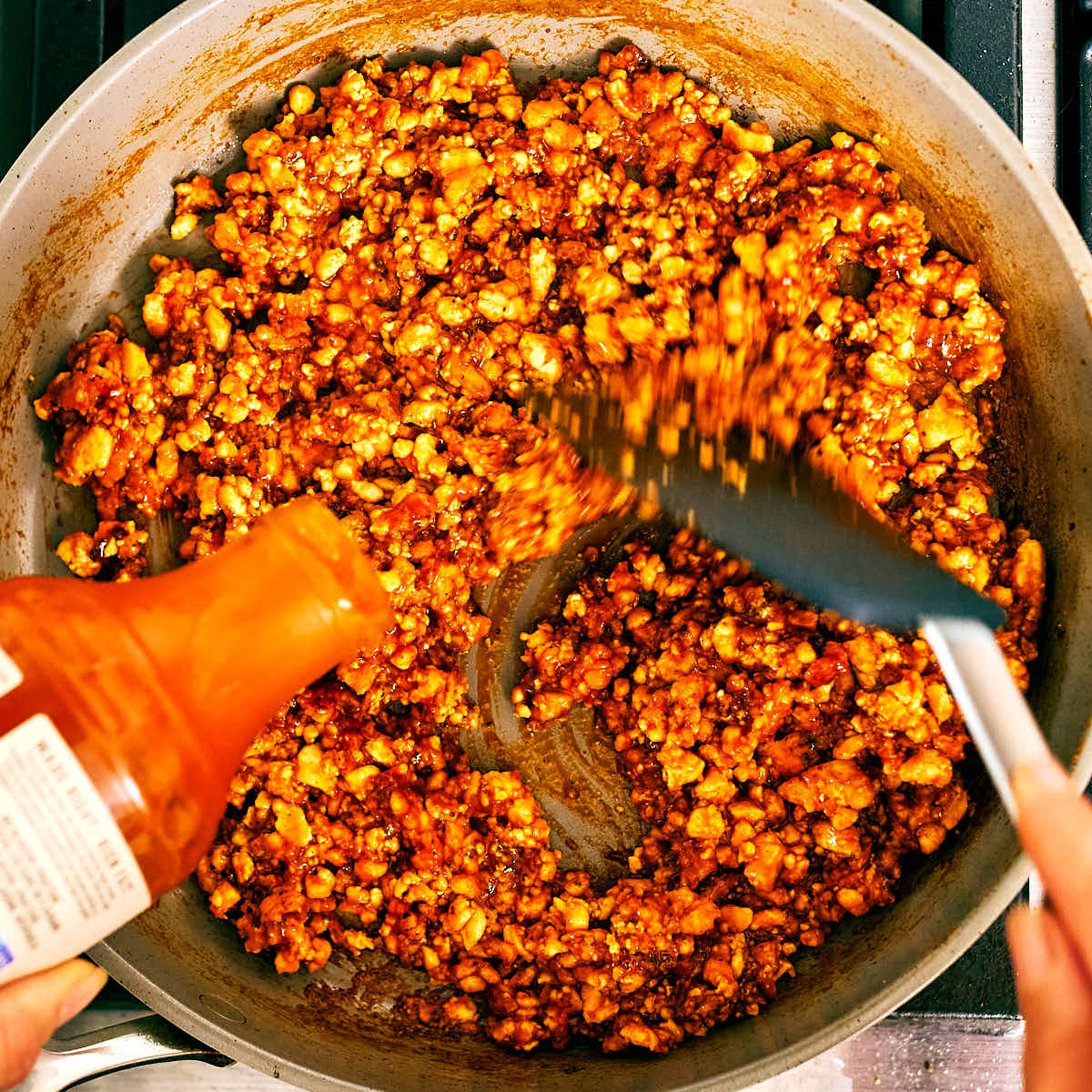 Barbecue sauce being poured into a skillet of crispy tofu for tacos.