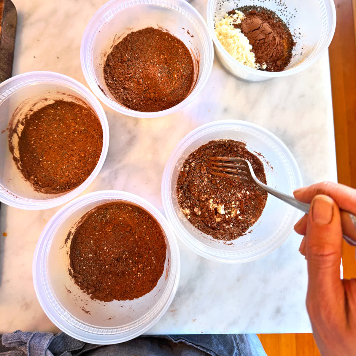 Chocolate Chia Pudding being meal prepped in deli cups on a marble counter.