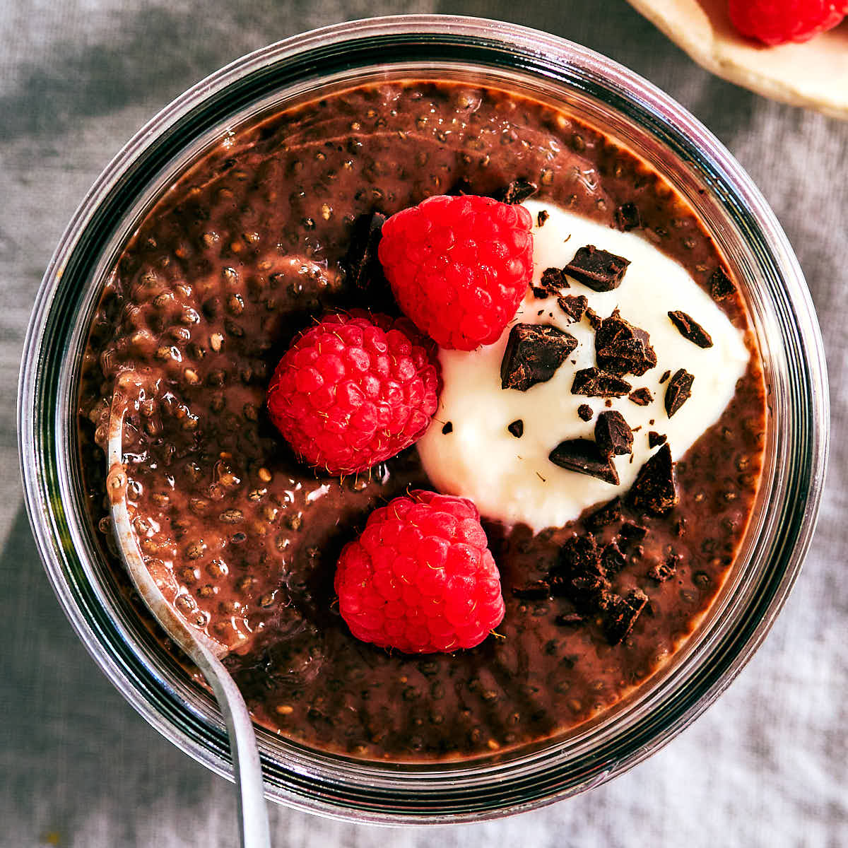 A spoon in a jar of high protein chocolate chia pudding with berries.