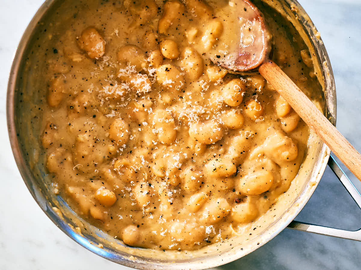 Creamy Cacio e Pepe Butter Beans in a skillet with a wooden spoon.