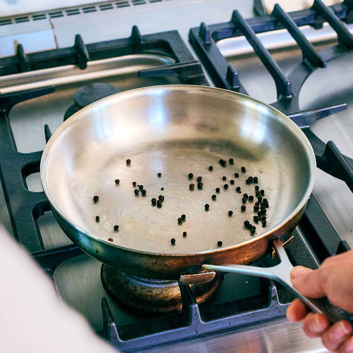 Whole peppercorns being toasted in a skillet on the stove.