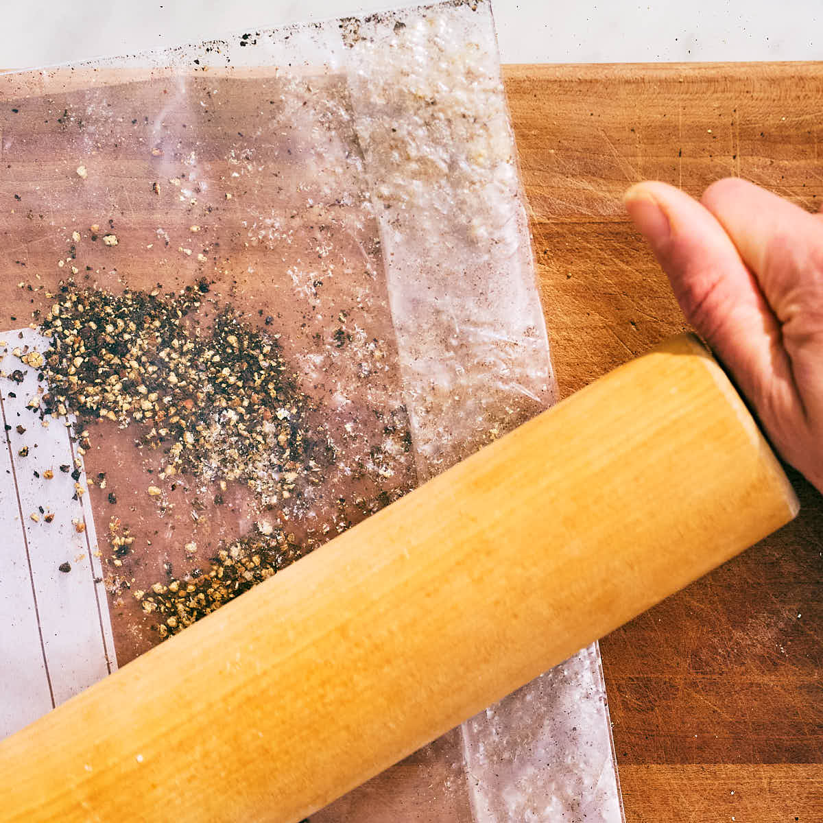 Toasted peppercorns being crushed by a rolling pin for Cacio e Pepe.