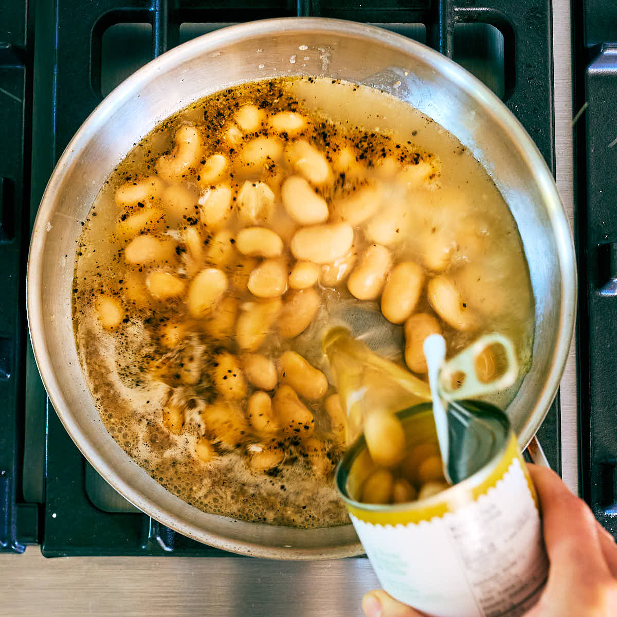 Butter beans and liquid being poured into a skillet.