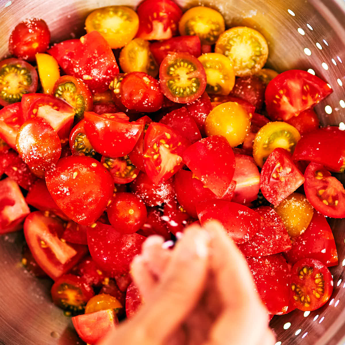 Tomatoes being salted in a strainer.