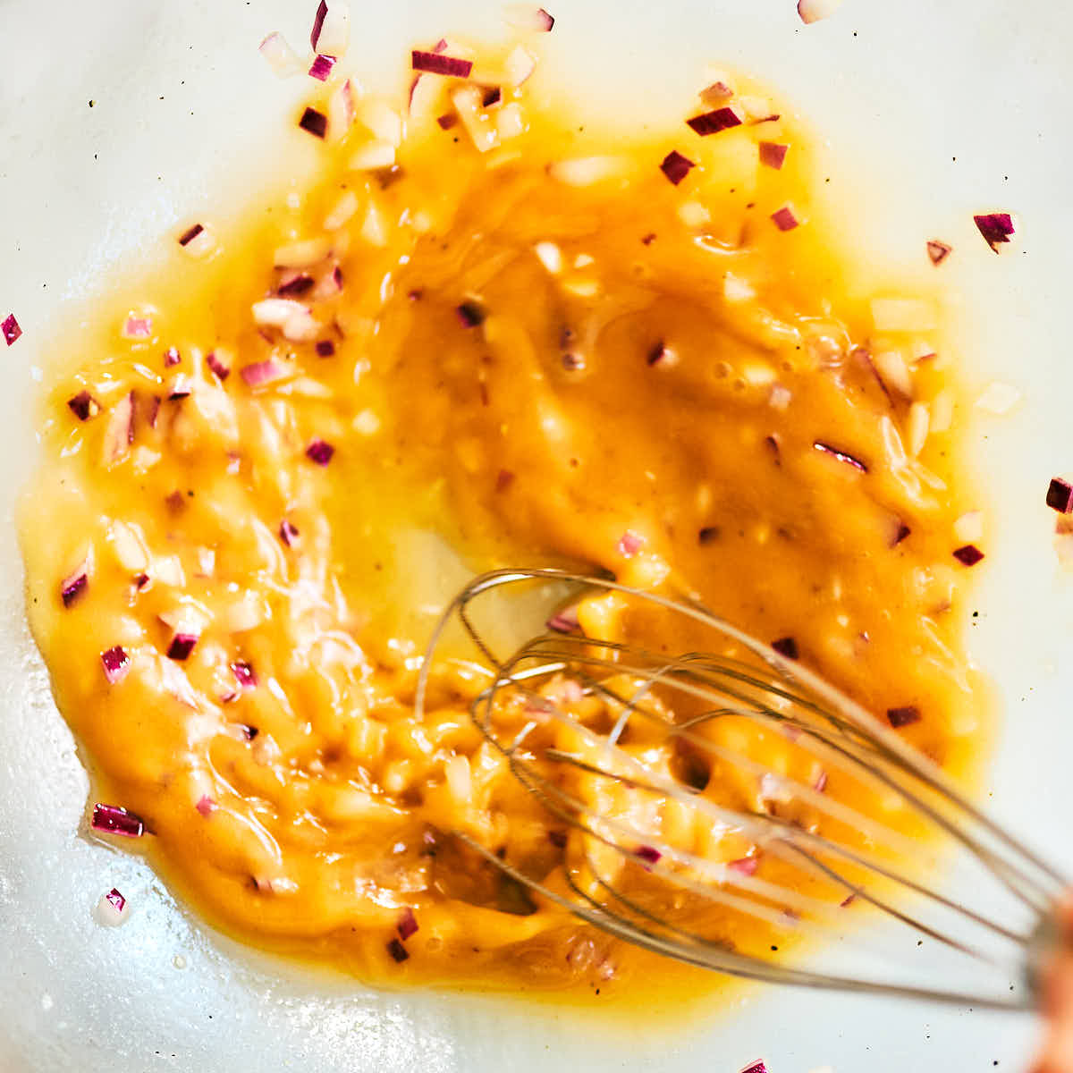 Dressing being whisked together in a bowl for tomato panzanella salad.