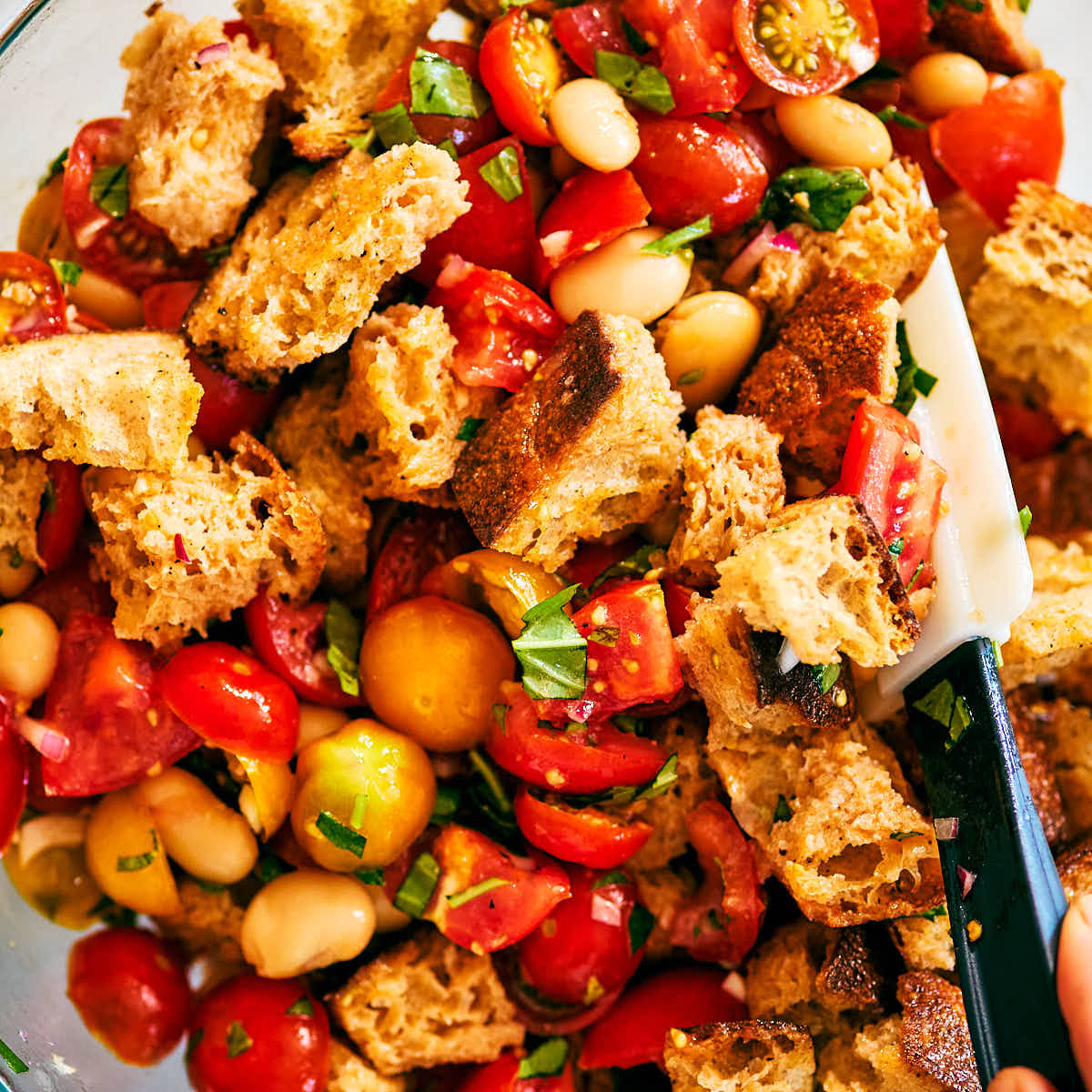 Evergreen Kitchen's Tomato Panzanella Salad being stirred in a glass bowl.