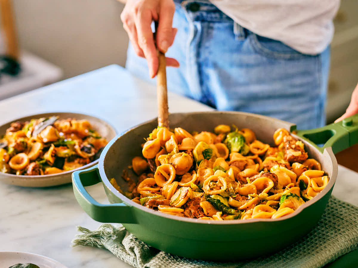 Brussels sprouts pasta being stirred in a skillet with a wooden spoon.