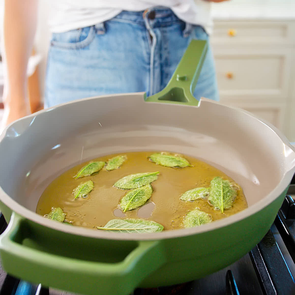 Sage leaves being fried in a skillet with olive oil.
