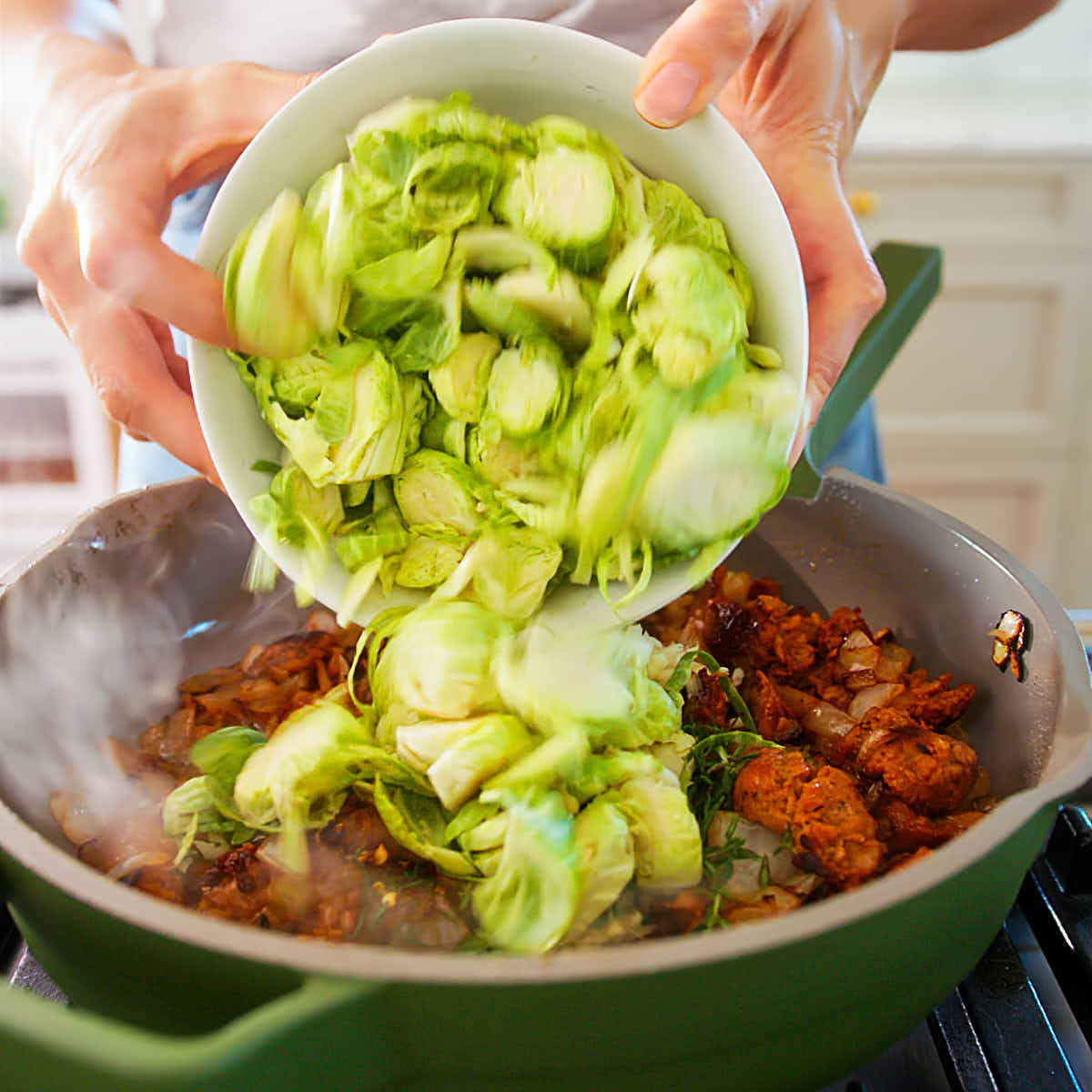 Thinly sliced brussels sprouts being added to a skillet for pasta.