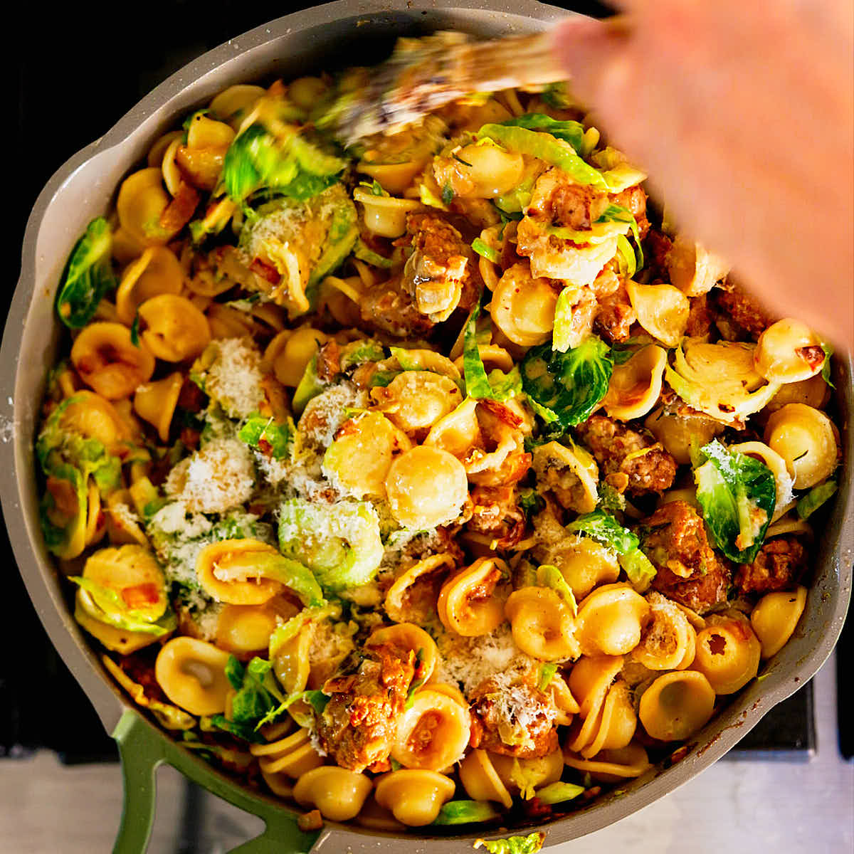 Brussels sprouts pasta with vegetarian sausage being cooked in a skillet on the stove.
